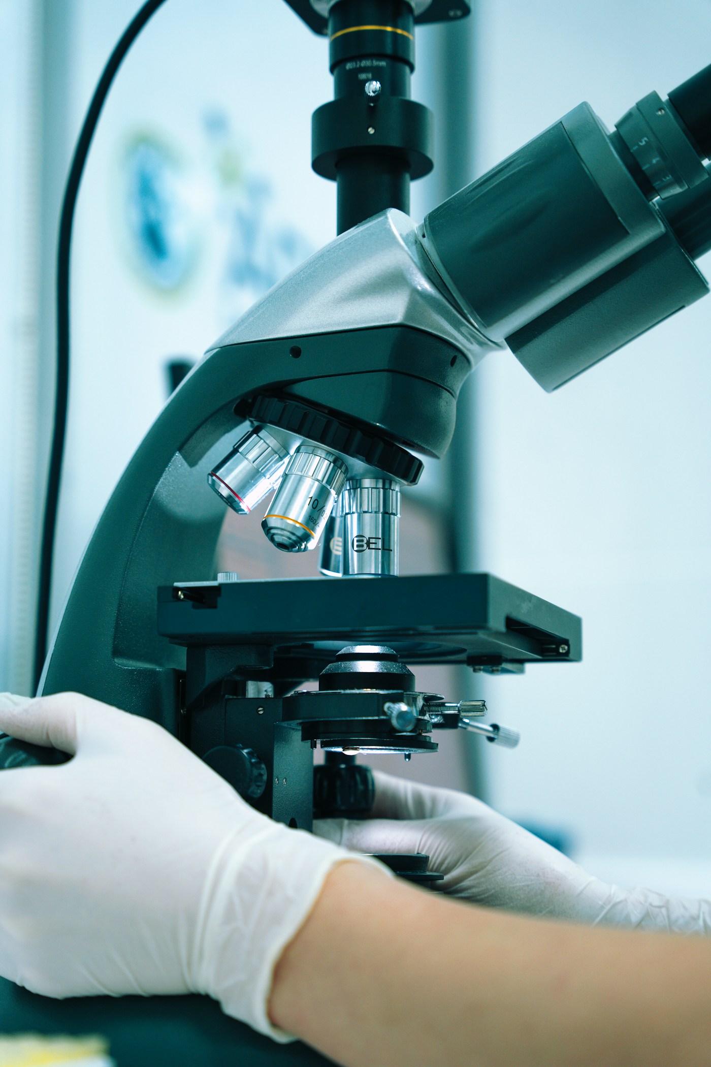 Close-up of a laboratory microscope with a gloved hand adjusting the controls
